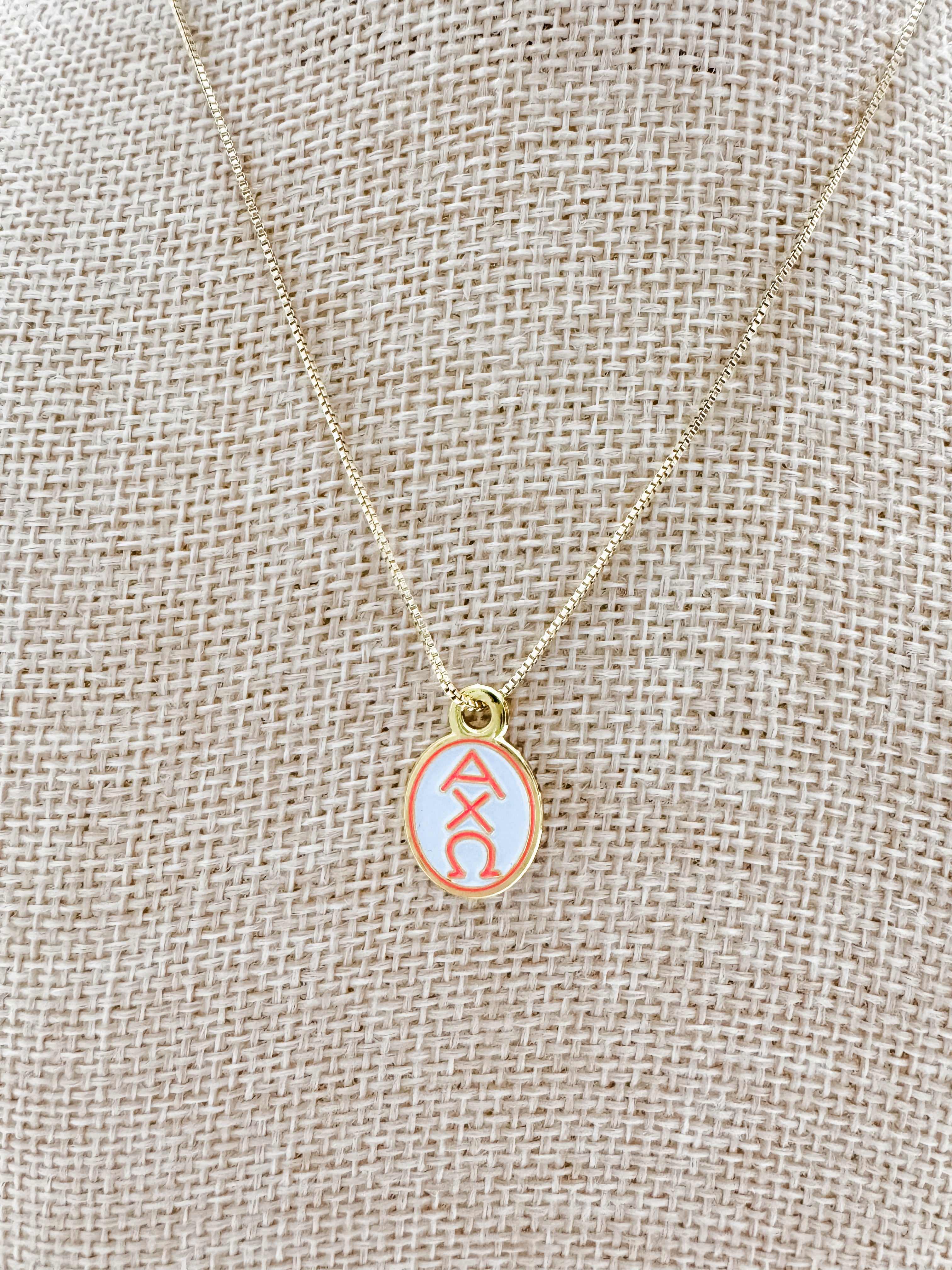 Alpha Chi Omega enamel pendant necklace on a beige fabric background
