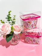 Two retail packages with floral designs on a pink surface with pink roses and green leaves for Alpha Phi sorority. 