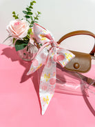 Handbag with a floral sorority silky tie on a pink surface with a vase of flowers.