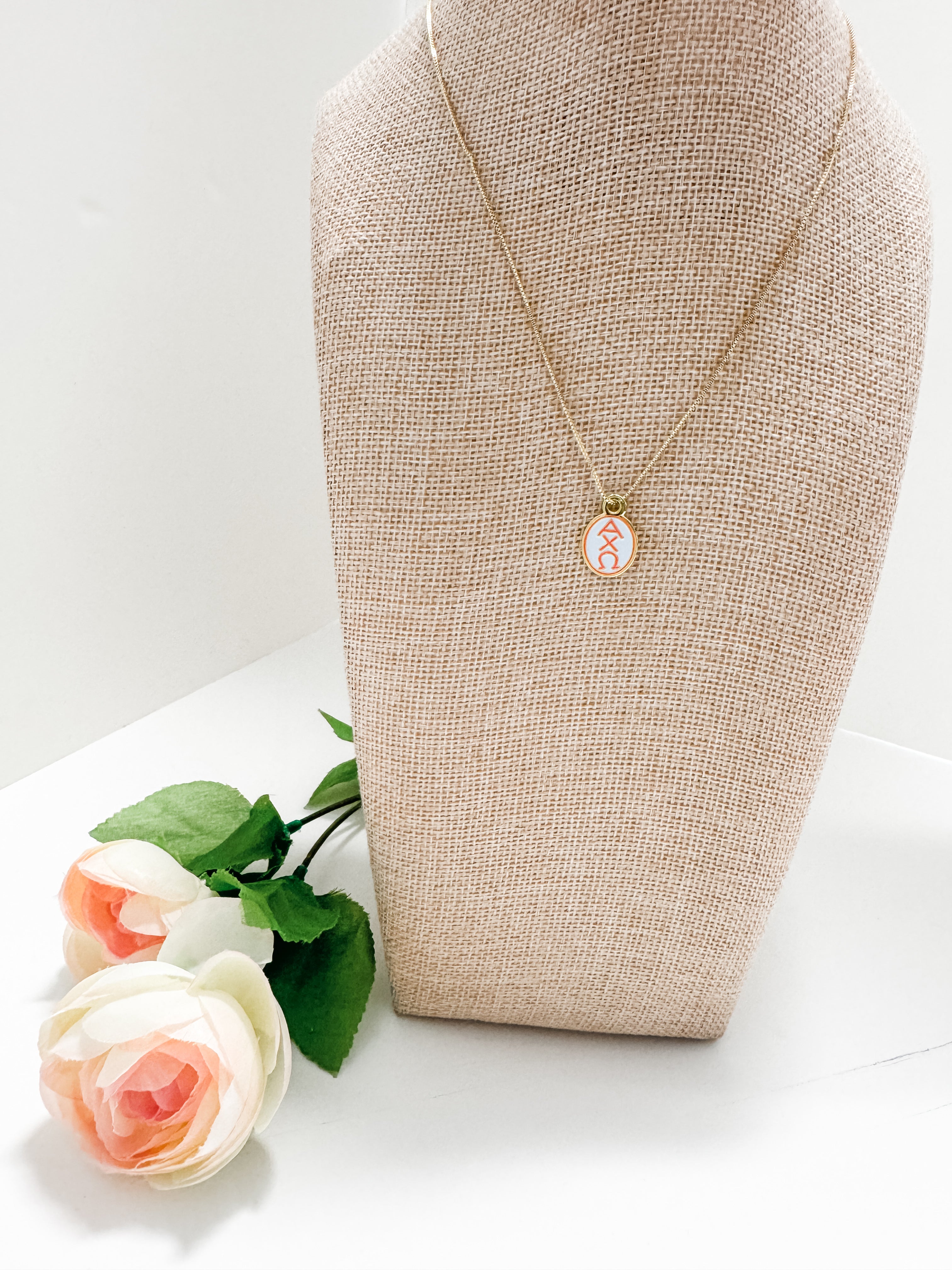 Alpha Chi Omega enamel pendant necklace on a mannequin bust with flowers on a white background