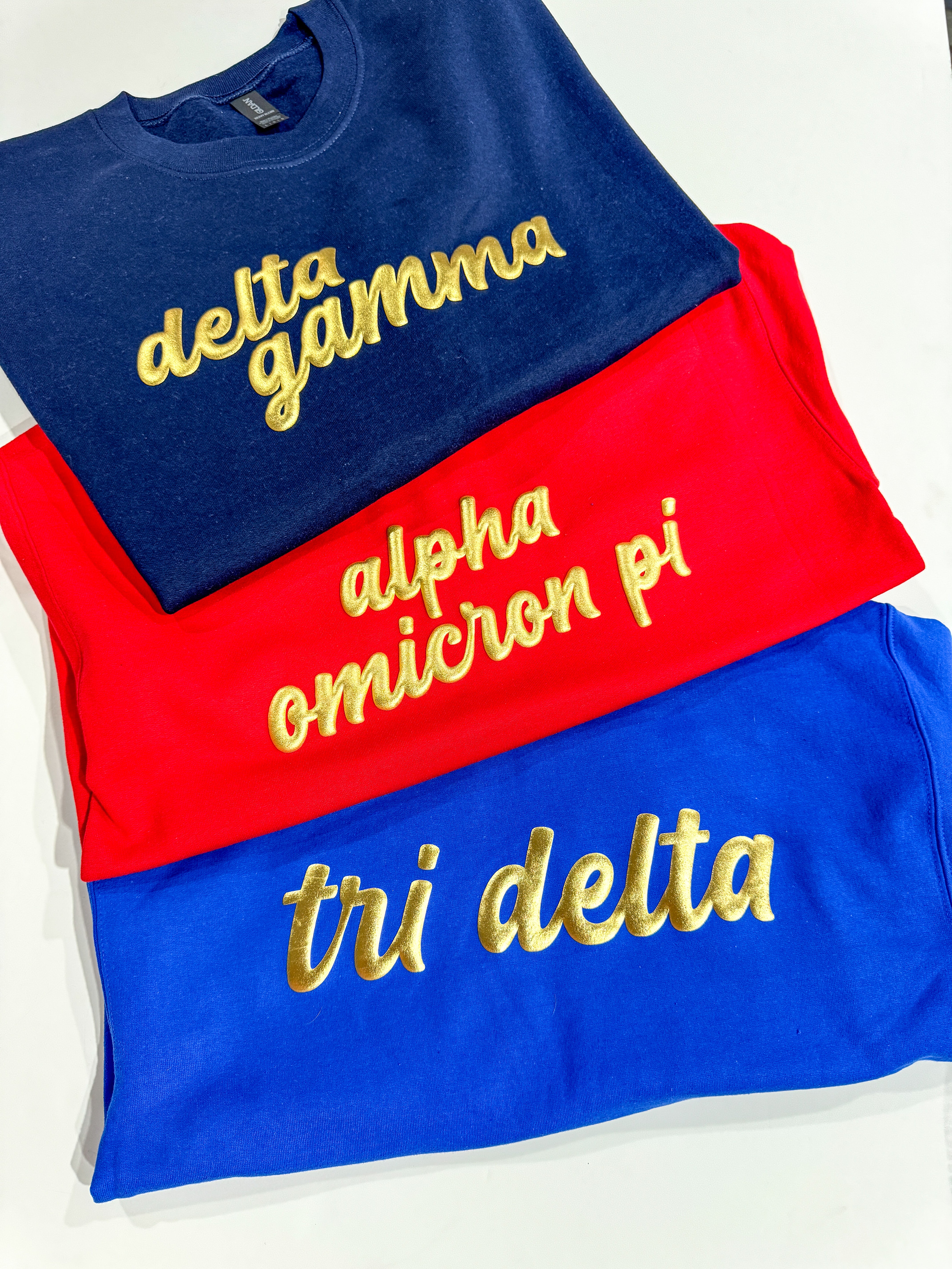 Sorority Greek gold puff sweatshirts with Delta Gamma, Alpha Omicron Pi, and Tri Delta designs